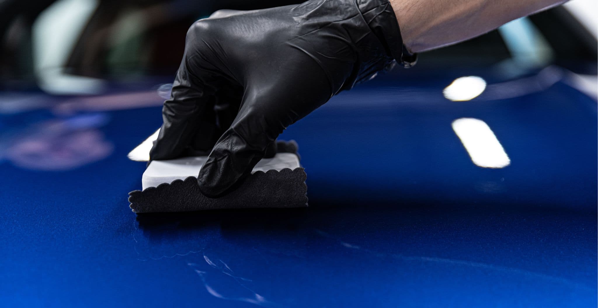 Technician applying ceramic coating to a car in Vancouver with a coating applicator